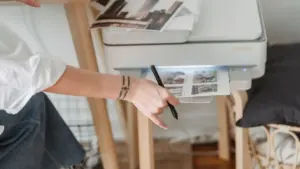 Frau druckt Fotos von einem Drucker, der neben dem Schreibtisch steht