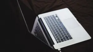 Laptop mit angeschlossenem Ladekabel auf dunklem Untergrund