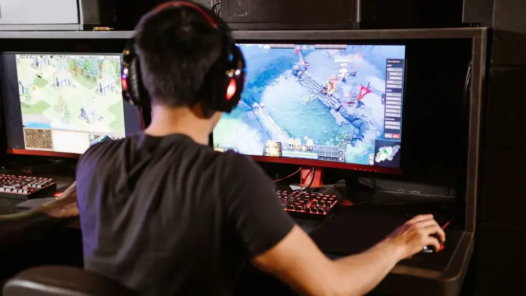 Person spielt am PC mit zwei Monitoren und Headset